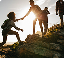 Group of friends walking up a hill, one friend is helping to pull another up